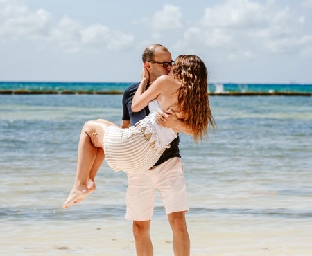 James Murray carrying and kissing girlfriend Melyssa Davies with an ocean view in the back.